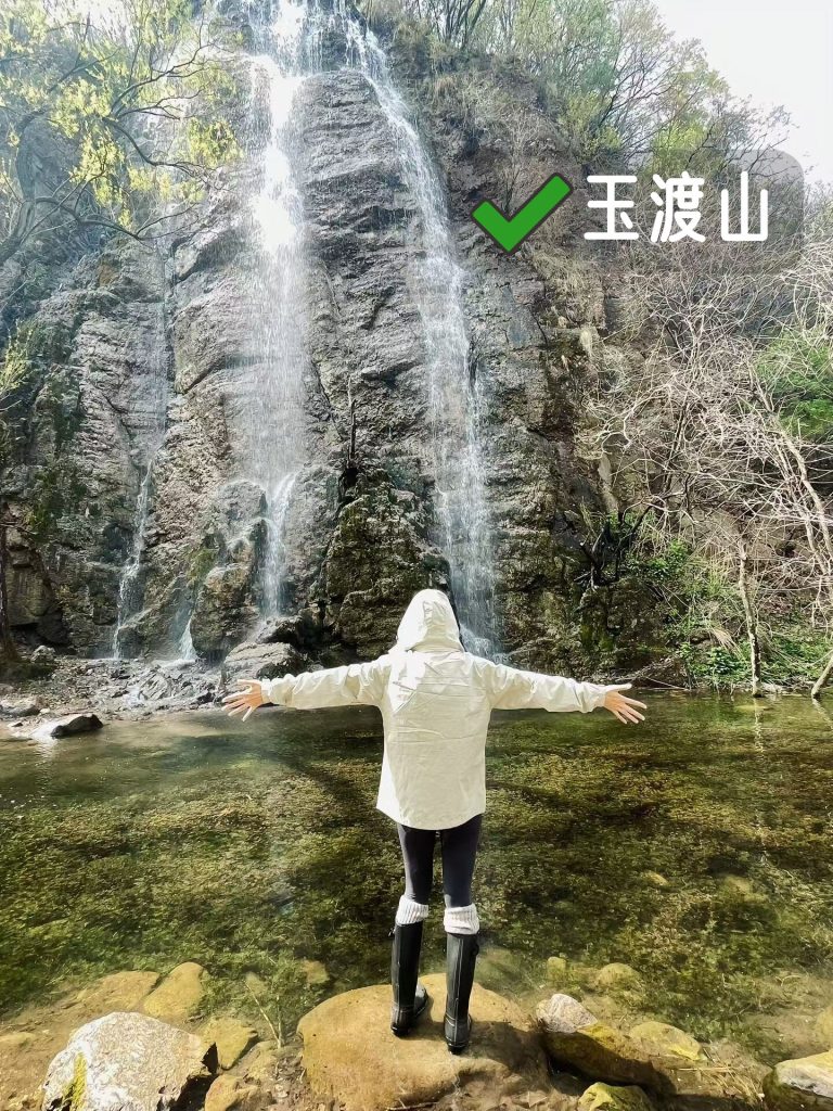Person posing before a waterfall with arms spread