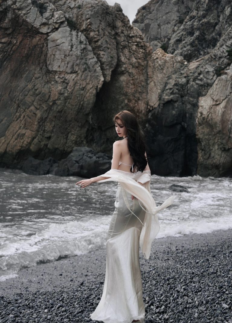 Woman in dress by rocky seaside