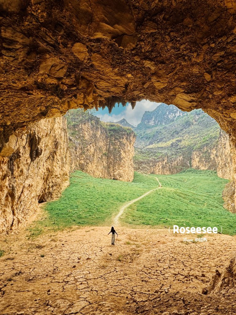 Person walking on a path outside a cave with mountains