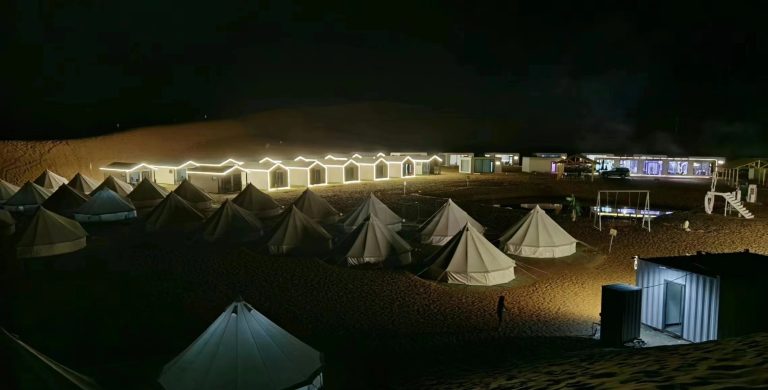 Desert camp at night with tents and lights