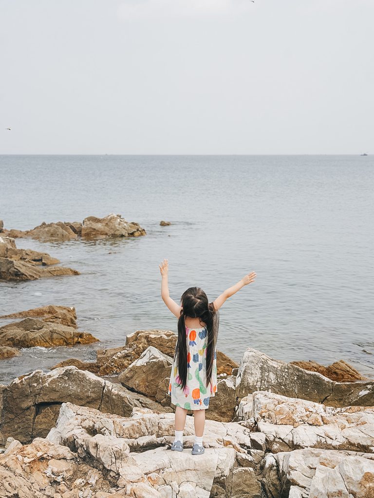 Child standing on seaside rocks with arms outstretched