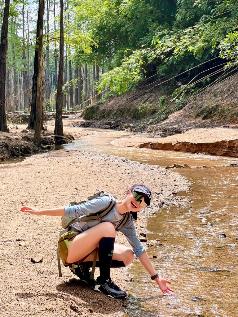 Person crouching by a forest stream, touching the clear water