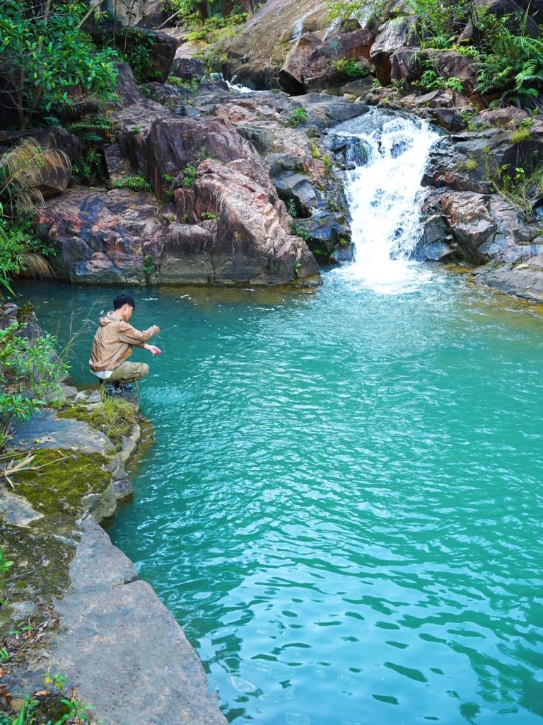 Person near a small waterfall and vibrant green pool in a forest
