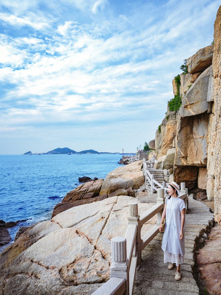 Woman in white dress standing on seaside steps overlooking the ocean
